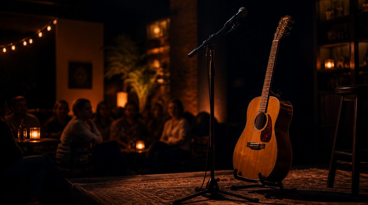 A guitar and microphone on a small stage, with an audience seated in candlelight behind